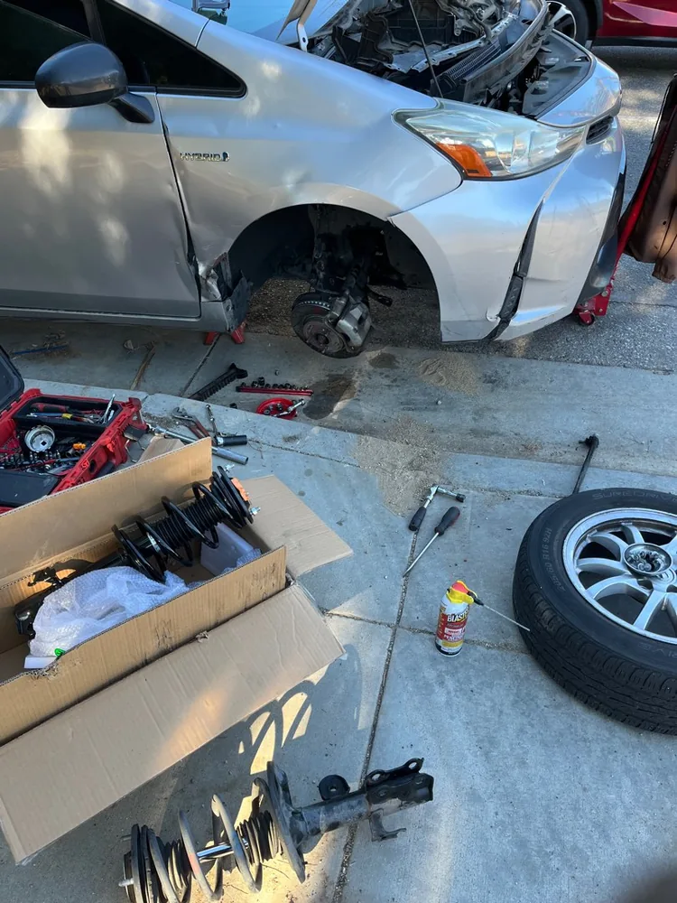 A car on a jack with the front wheel off and new springs in a box