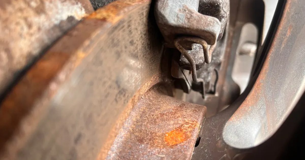 A rusted brake rotor and caliper bracket up close with the wheel off