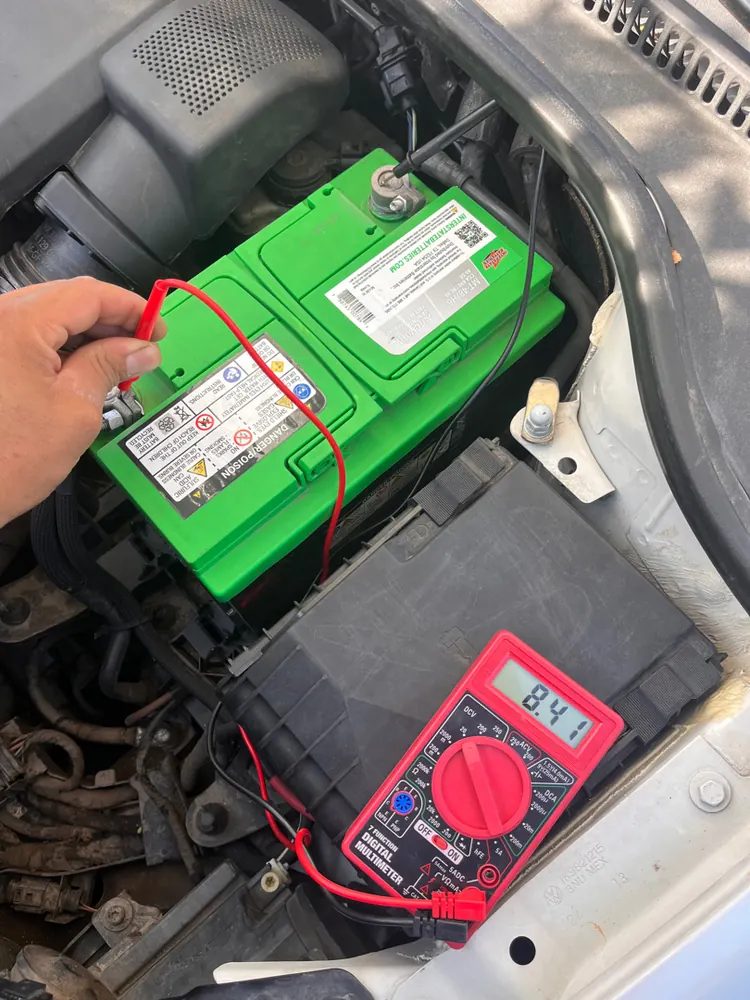 A multimeter wired to a car battery to measure a parasitic draw