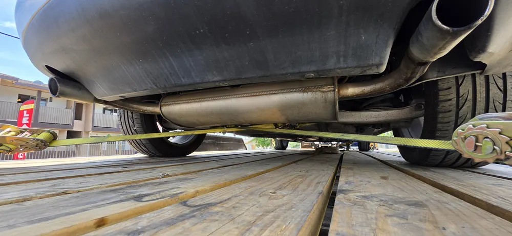 Yellow ratchet straps pulled tight across the wheels of a car on a wood deck trailer