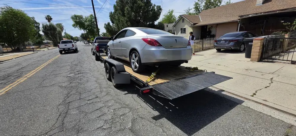 A silver Pontiac G6 on a car trailer pulled to the curb of a residential street