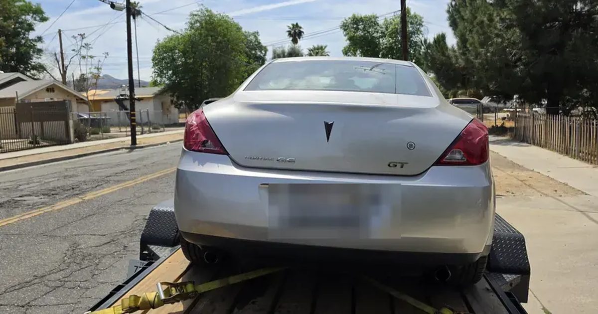 The back of a silver Pontiac G6 GT loaded on a car trailer on a residential street, plate blurred