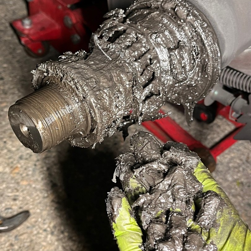 A gloved hand holding a fistful of old grease next to a bare spindle on a truck on a jack