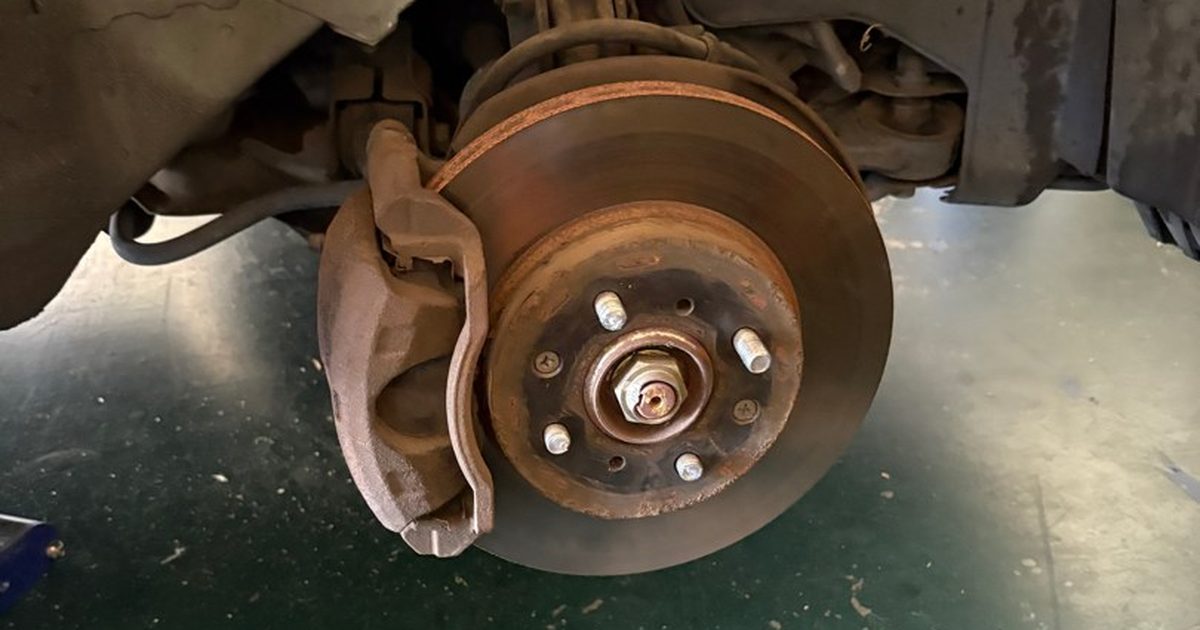 A front corner with the wheel off, showing a rusty brake rotor, the caliper and the axle nut in the center of the hub